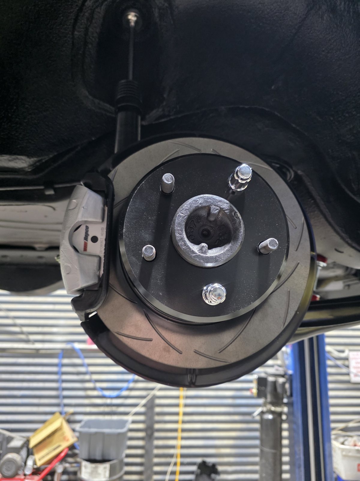 New slotted brake rotor and caliper fitted, seen from under a car on the hoist