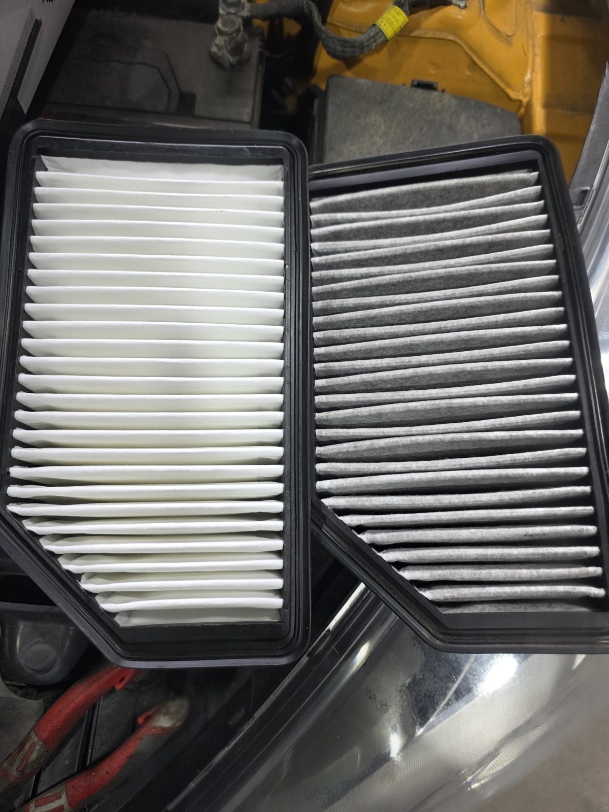 Two filters held side by side over an engine bay