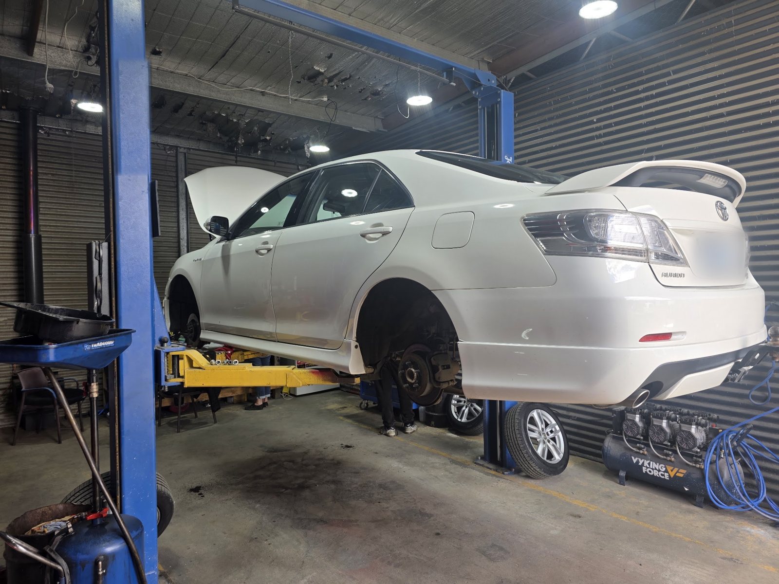A white Toyota Aurion up on the hoist in Tim’s workshop, rear wheel off